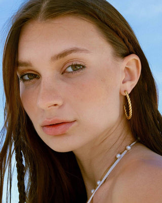 Detalle de argollas en trenza doradas en oreja de modelo, joya waterproof de Pialü
