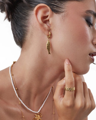 Vista de cerca de aretes dorados con colgante de pez grabado y brillo marino, waterproof de Pialü