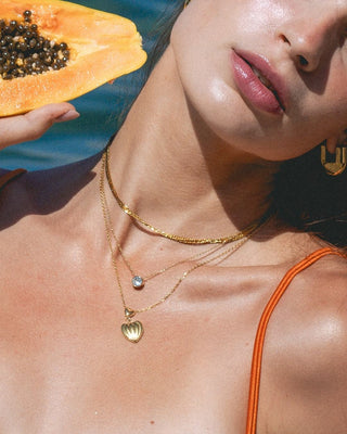 Modelo con collar dorado fino y colgante zircón redondo en cuello, joya waterproof Pialü
