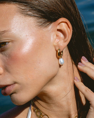 Modelo luciendo aros dorados con perla barroca en oreja, joya waterproof de Pialü