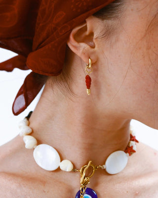 Detalle de aretes marineros con dije rojo en relieve dorado, waterproof de Pialü
