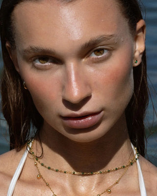 Aretes stud esmeralda dorados sobre superficie blanca, ángulo superior, waterproof Pialü