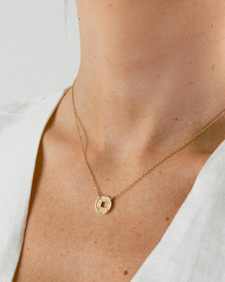 Collar plateado con dije moneda sobre fondo claro, acero inoxidable Pialü