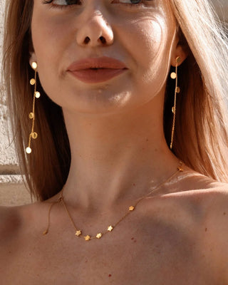 Vista lateral de aretes dorados con múltiples discos dorados a lo largo de cadena, joya Pialü