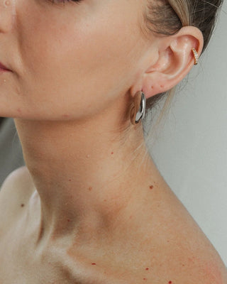 Vista lateral de aretes de caracola plateada con acabado espejo, joya acero inoxidable Pialü